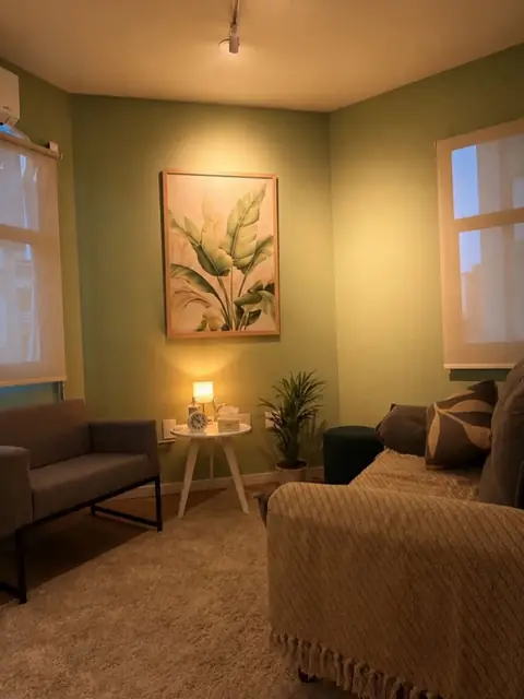 Sala aconchegante com poltronas, manta sobre o sofá, abajur aceso, planta e quadro de folhagem