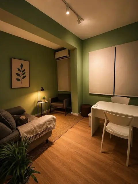 Sala reservada com mesa e cadeiras brancas, sofá com manta, quadro de folha e luz quente