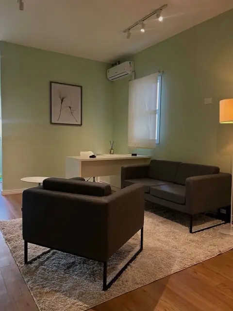 Sala de atendimento com poltrona e sofá cinza, quadro minimalista e janela com cortina