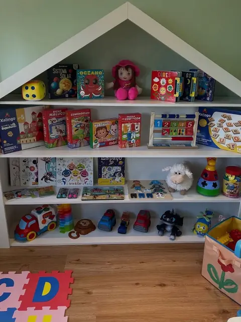 Estante em formato de casinha com livros, jogos pedagógicos e brinquedos organizados por prateleira