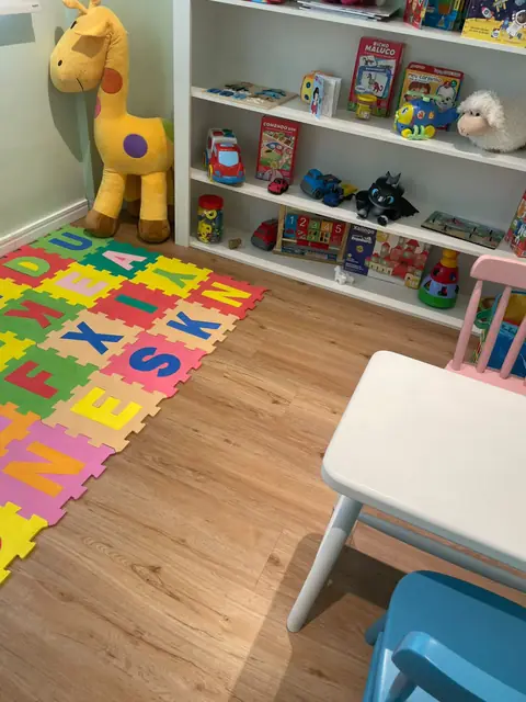 Canto da sala infantil com girafa de pelúcia, estante de livros e tapete de letras coloridas