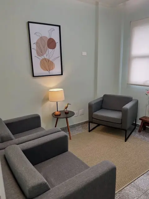 Canto de espera com poltronas, abajur e quadro de folhas em tons terrosos